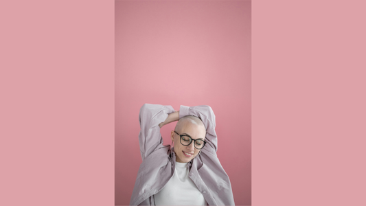 Femme souriante au crâne rasé assumé posant avec confiance sur fond rose, symbole de résilience, de féminité retrouvée et d'acceptation de soi.