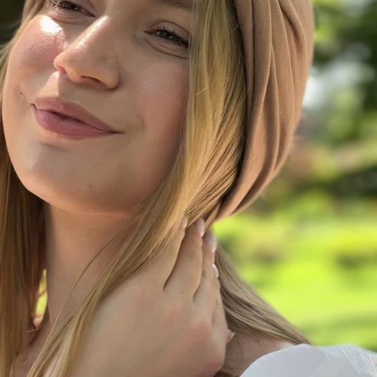 Turban Maison Dunel Nude chic et léger, porté par une femme souriante en extérieur verdoyant