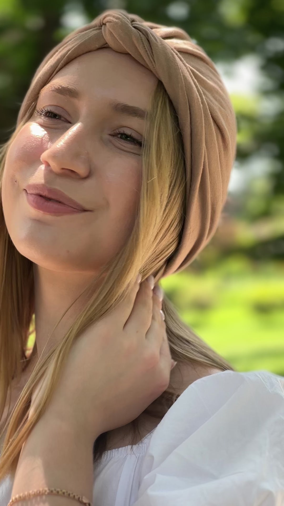 Turban Maison Dunel Nude chic et léger, porté par une femme souriante en extérieur verdoyant